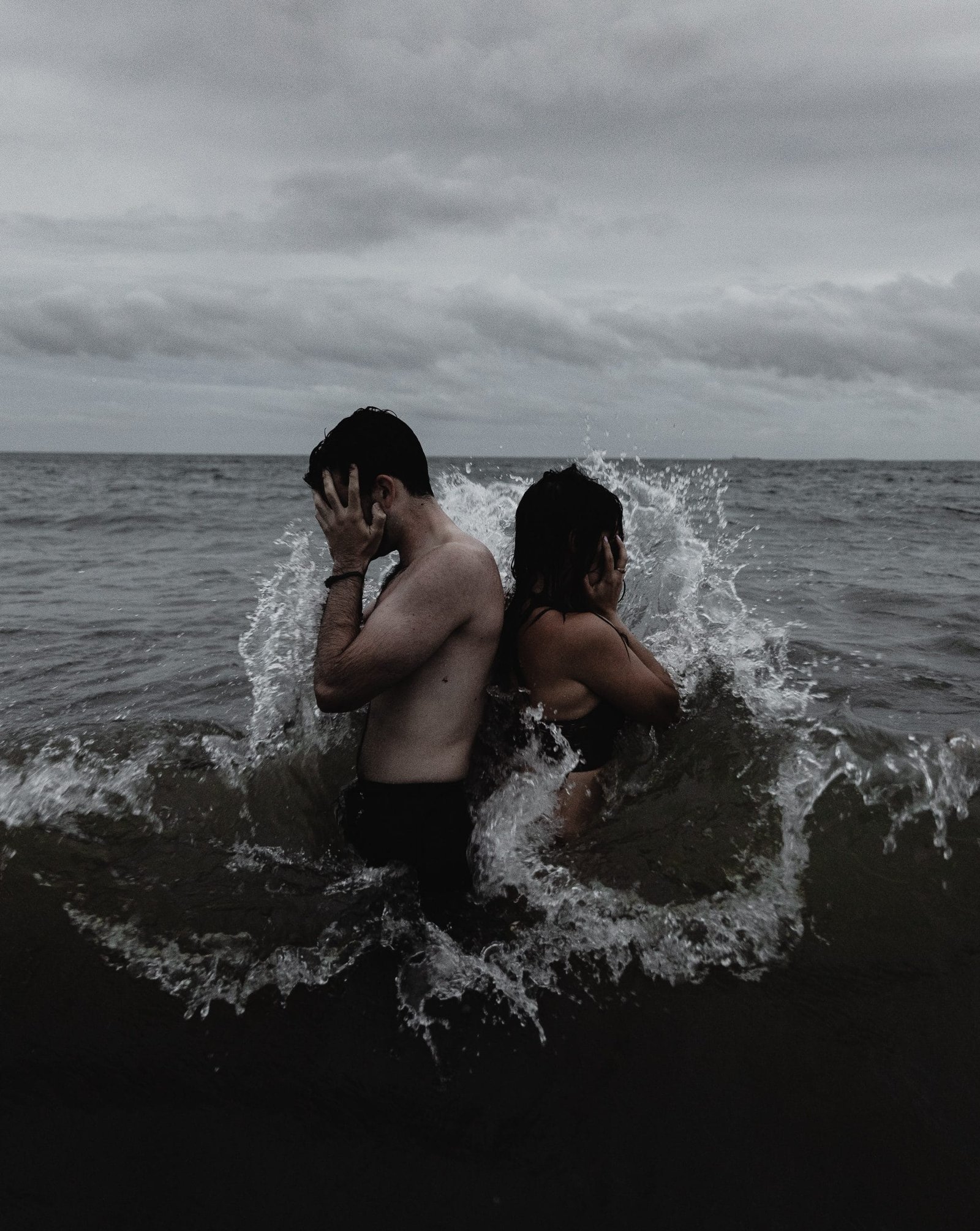 man and woman facing away from each other in water while covering their faces with their hands