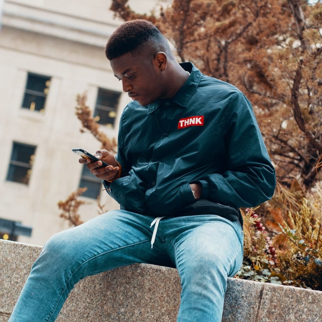 black man sitting on wall staring down at phone intensely