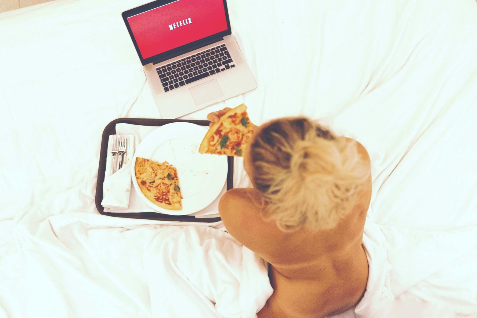 woman naked in bed eating pizza and watching netflix on laptop